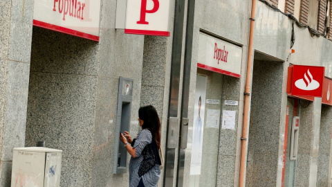 Una foto de junio de 2017 de una mujer utilizando el cajero automático de una oficina del extinto Banco Popular, junto a otra sucursal del Banco Santander. REUTERS/Albert Gea