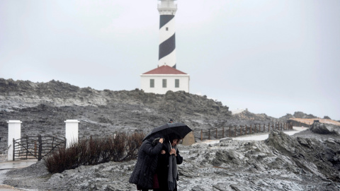 Dos personas caminan por las inmediaciones del faro de Faváritx, en el municipio de Mahón, en una jornada en la que la borrasca Gloria, que trae este domingo un temporal de lluvia, nieve, viento y olas, ha puesto en alerta roja a la Comunidad Valenciana