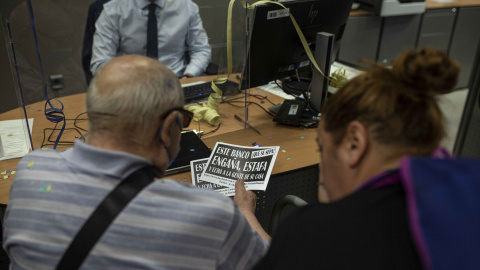 Un cliente de CaixaBank observa uno de los panfletos repartidos por los activistas durante su protesta contra varios desahucios den banco en el distrito.