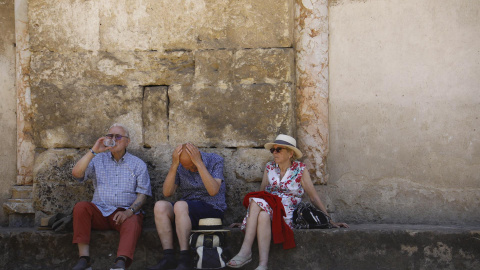 Unos turistas descansan y beben agua sentados a la sombra en los alrededores de la Mezquita-Catedral en Córdoba