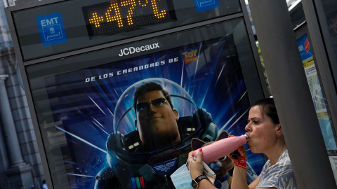 Una mujer bebe agua en la sombra de una parada de autobús de Madrid cuyo termómetro marca 47ºC.