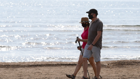 Dos personas protegidas con mascarilla pasean por la playa de la Malvarrosa durante su franja horaria permitida en la desescalada ante la crisis del Covid-19 en la que mayores de 14 años y menores de 69 tienen permitidas las salidas para pasear y hacer d