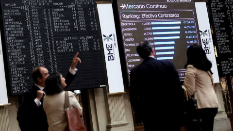 Cuatro personas frente a un panel de valores del Ibex 25 en el Palacio de la Bolsa, a 30 de mayo de 2022, en Madrid.