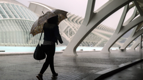 Una mujer se refugia de la lluvia con un paraguas en la Ciudad de las Ciencias de València./EFE