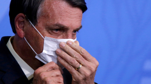 El presidente de Brasil, Jair Bolsonaro, ajustándose la mascarilla.