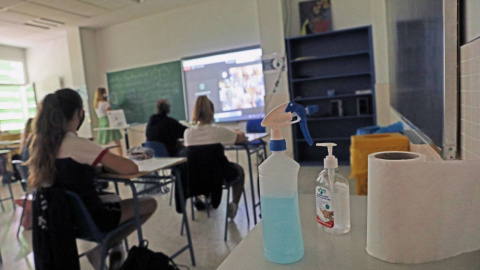 Productos desinfectantes colocados en los pupitres desde donde los alumnos atienden a las clases semipresenciales impartidas en el Colegio Ábaco, en Madrid.