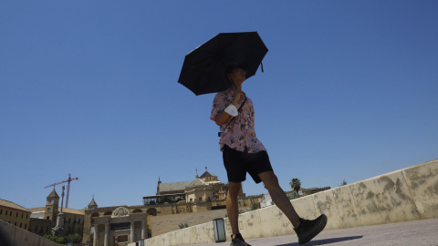 (10/6/2022) Un turista se protege del sol con un paraguas a su paso por el Puente Romano con la Mezquita-Catedral de Córdoba.