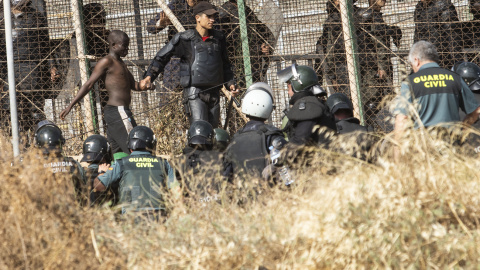 Un miembro de las fuerzas de seguridad marroquí se lleva detenido a un migrante desde el lado español de la frontera con Melilla.