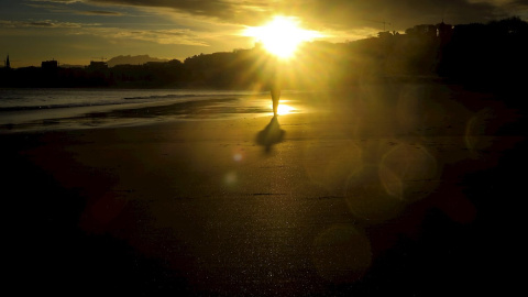 Un hombre observa el amanecer en la playa de Ondarreta de San Sebastián.