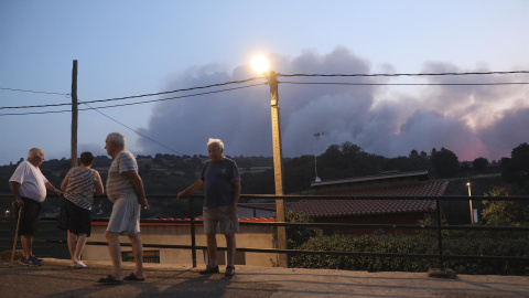 Varios vecinos observan la columna de humo del incendio forestal declarado en Monsagro, desde la localidad salmantina de Serradilla del Arroyo, en la madrugada de este viernes.