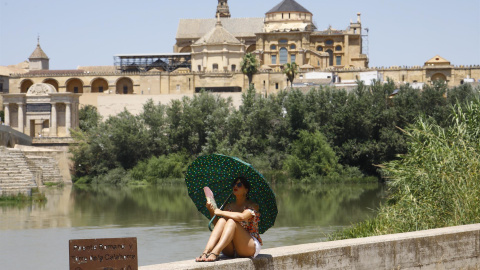 11/07/2022-Una turista se protege del calor con un paraguas y un abanico a la orilla del río Guadalquivir cerca de la Mezquita-Catedral de Córdoba este lunes cuando la Agencia Estatal de Meteorología (Aemet), ha alertado que la segunda ola de calor de 