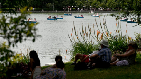 La gente se sienta a la sombra de los árboles mientras otros reman en botes en el Parque del Retiro en el centro de Madrid en la ola de calor de junio de 2022.