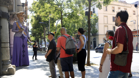 Un home espera amb una rosa per entrar a la capella ardent de Núria Feliu i observa la geganta de l'artista, a les portes del districte de Sants-Montjuïc, a Barcelona.