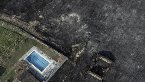 Fotografía tomada con un dron de una piscina y una construcción rodeadas por la superficie calcinada en el pueblo de San Cibrao, Oímbra, Ourense.