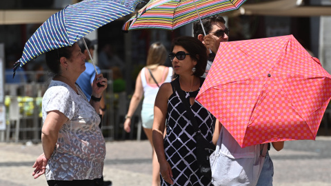 Varias personas caminan con sombrilla por el centro de Madrid.