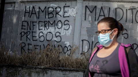 Una mujer camina frente a una pared con un graffiti pintado que dice "Hambre, enfermos, presos, refugiados" el 8 de febrero de 2021, en Caracas (Venezuela).