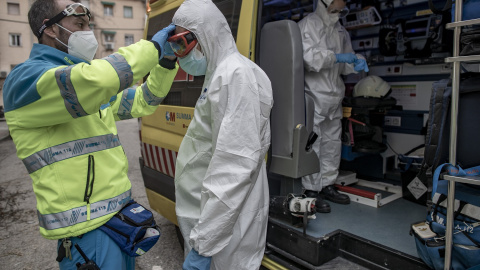 Un trabajador de una UVI móvil del SUMMA 112 se viste con un EPI con la ayuda de otro trabajador durante una jornada de trabajo, en Madrid.