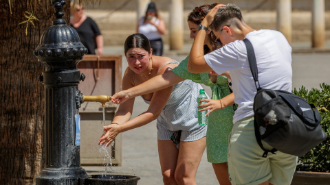 Unas turistas se refrescan en una fuente de agua junto a la Catedral de Sevilla hoy viernes a mediodía.- EFE/Julio Muñoz