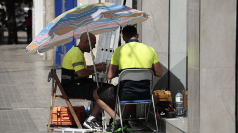 Dos operarios de telefonía se protegen con una sombrilla del intenso sol y calor en Valencia.