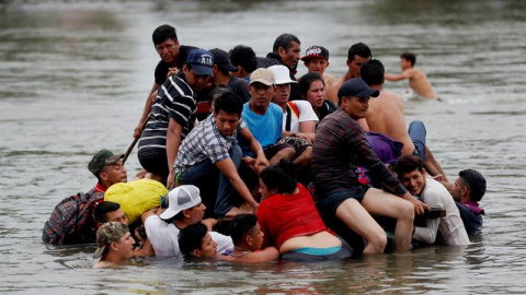 Decenas de migrantes hondureños cruzan a pie y el balsa el río Suchiate, que separa a Guatemala de México, mientras otros observan desde un puente. EFE/Esteban Biba