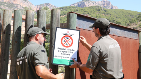 Dos Agents Rurals col·loquen un cartell informatiu a l'accés al Parc Natural de la Serra de Montsant des de la Cartoixa d'Escaladei.