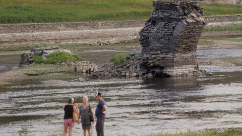 Tres personas junto al río Miño, cuyo bajo caudal ha dejado a la vista las ruinas del antiguo Portomarín, que en los años 60 del siglo pasado fue anegado por el embalse de Belesar