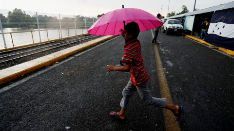 Alex corre bajo la lluvia en el puente de la frontera entre Guatemala y México. EFE/ESTEBAN BIBA