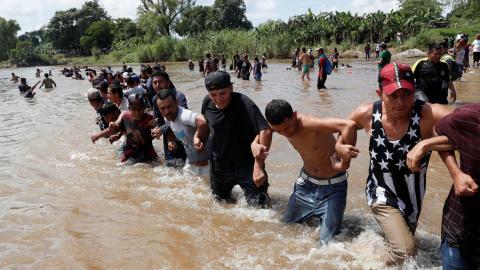 Decenas de personas de la caravana de centroamericanos se unen entre ellas para poder atravesar el río Suchiate, la frontera natural entre Guatemala y México. | Leah Millis / Reuters