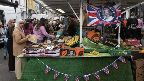 Día de mercado, una mujer mira a la cámara desde un puesto de frutas en la periferia londinense.