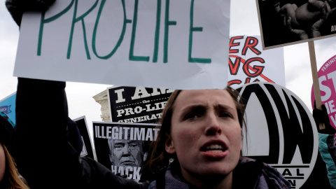 A fondo, una contramanifestante sostiene un cartel anti Trump. / Reuters