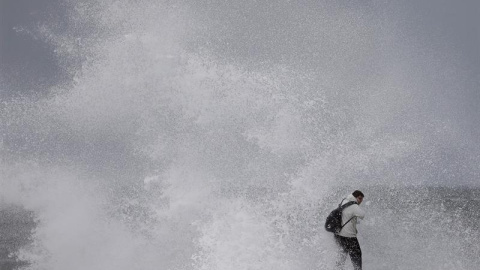 Un ciudadano desafía el fuerte oleaje en la playa de Barceloneta, durante el temporal marítimo que afecta a toda la costa catalana. EFE/ Andreu Dalmau