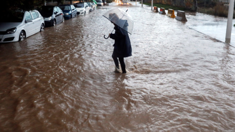 Una persona cruza una calle inundada durante la tarde del viernes en la que el temporal de lluvia torrencial ha azotado por tercera jornada consecutiva la provincia de Valencia. EFE/Kai Försterling