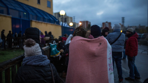 Una pareja de solicitantes de asilo se abriga con una manta mientras hace cola para pedir cita en la comisaría de Aluche. Algunos llevan 48 horas esperando su turno bajo el frío y la lluvia. JAIRO VARGAS