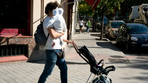 Un hombre cuida de su hijo por las calles de Madrid.