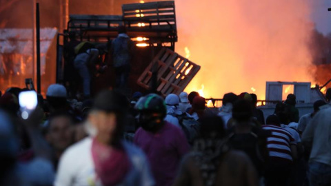 Manifestantes se enfrentan con miembros de la Policía Nacional Bolivariana, junto a un camión que transportaba ayuda humanitaria y fue quemado, este sábado, en el puente Francisco de Paula Santander, en la frontera entre Cúcuta (Colombia) y Venezuela.