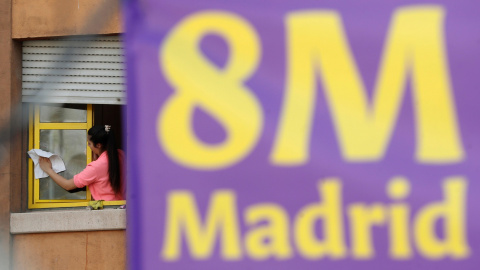 Una mujer limpia una ventana junto a un cartel alusivo al Día Internacional de la Mujer, este viernes en Madrid. EFE/Chema Moya