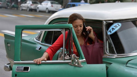 Una mujer toma un taxi co un viejo automóvil estadounidense en una calle de La Habana. AFP/Yamil Lage