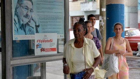 Una mujer pasa junto a un cartel del ex presidente cubano Raúl Castro y un cartel de la campaña del gobierno que lee "#Ivoteyes" en referencia a la nueva Constitución, aprobada recientemen en referéndum. APF/Yamil Lage