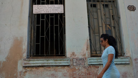 Una mujer camina junto a una vivienda con un cartel de "En venta" en La Habana. AFP/Yamil Lage