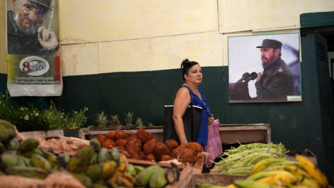 Una mujer compra verduras junto al póster del difunto líder cubano Fidel Castro en un mercado en La Habana. AFP/Yamil Page