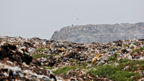 Un hombre recolecta materiales reciclables a medida que el humo se acumula en un vertedero en llamas con motivo del Día de la Tierra, en Calcuta. / Reuters