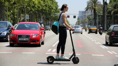 Una joven cruza un paso de peatones con un patinete eléctrico.