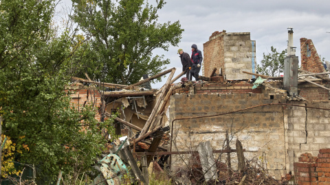 Ciudadanos limpian los escombros de un edificio dañado por los bombardeos en la aldea de Ruski Tyshky del área de Kharkiv.