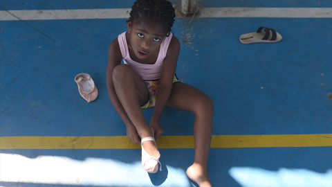 Una niña intenta atarse su zapato para ir a la escuela.