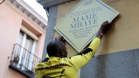 15/03/2019.- Un hombre coloca un placa durante la concentración convocada por el Sindicato de Manteros esta tarde en la plaza de Nelson Mandela, en Madrid, en recuerdo a Mame Mbaye, cuando se cumple un año de la muerte por un infarto de este vendedor se