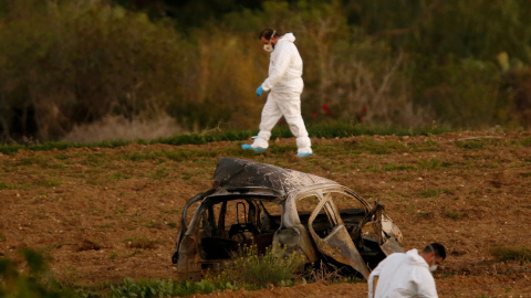 Expertos forenses caminan en un campo después de que una bomba explotara un automóvil (primer plano) y matara a la periodista de investigación Daphne Caruana Galizia en Bidnija, Malta, el 16 de octubre de 2017