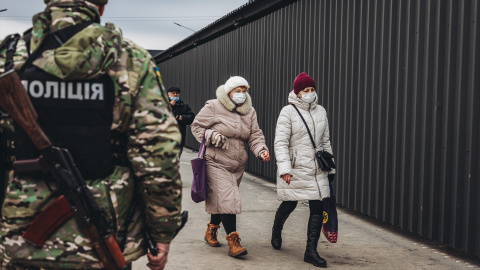 Dos mujeres caminan delante de un policía en el control fronterizo de Stanitsa Luganska para cruzar del territorio ucraniano al territorio de la autoproclamada República de Lugansk, a 17 de febrero de 2022, en Stanitsa Luganska, Oblas de Lugansk (Ucrani