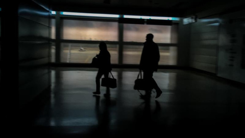 Dos personas caminan este miércoles por un pasillo del aeropuerto internacional "Simón Bolívar" totalmente a oscura. /MIGUEL GUTIÉRREZ (EFE)