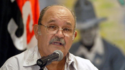 Miguel D'Escoto, ofreciendo una charla delante de la bandera del Frente Sandinista de Liberación Nacional y la imagen del líder nicaragüense Augusto Sandino.