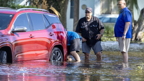 Varias personas intentan mover un automóvil averiado en una calle inundada tras la llegada del huracán Milton a tierra en Clearwater, Florida, EE.UU., el 10 de octubre de 2024.